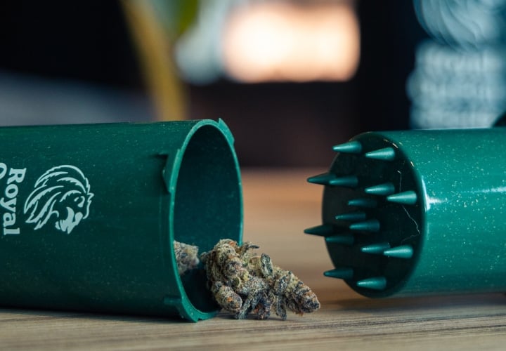 Grindtainer para guardar y triturar cannabis fácilmente Imagen de un grindtainer compacto con cogollos de cannabis sobre una superficie de madera.