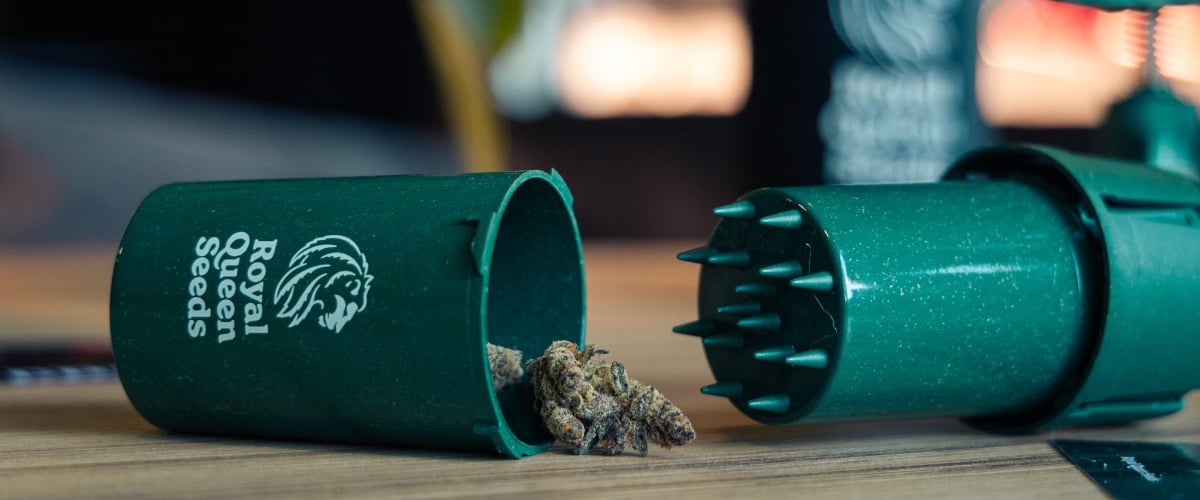 Grindtainer para guardar y triturar cannabis fácilmente Imagen de un grindtainer compacto con cogollos de cannabis sobre una superficie de madera.