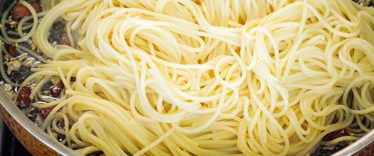 Espaguetis escurridos mezclados con panceta crujiente y mantequilla infusionada en una sartén, cuarto paso para una carbonara con cannabis