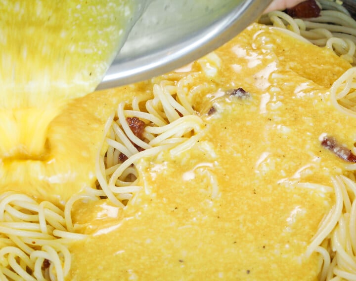 Vertiendo la mezcla de huevo y queso sobre espaguetis calientes en una sartén, quinto paso para una carbonara infusionada con cannabis